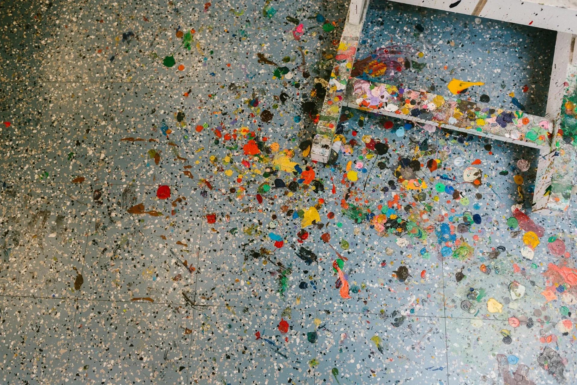 Un sol d’atelier constellé de centaines de taches de peinture de toutes les couleurs, au pied d’un chevalet.